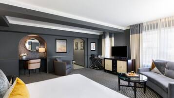 Habitación de hotel con una cama grande, un sofá, un escritorio con silla, un televisor y un minibar.