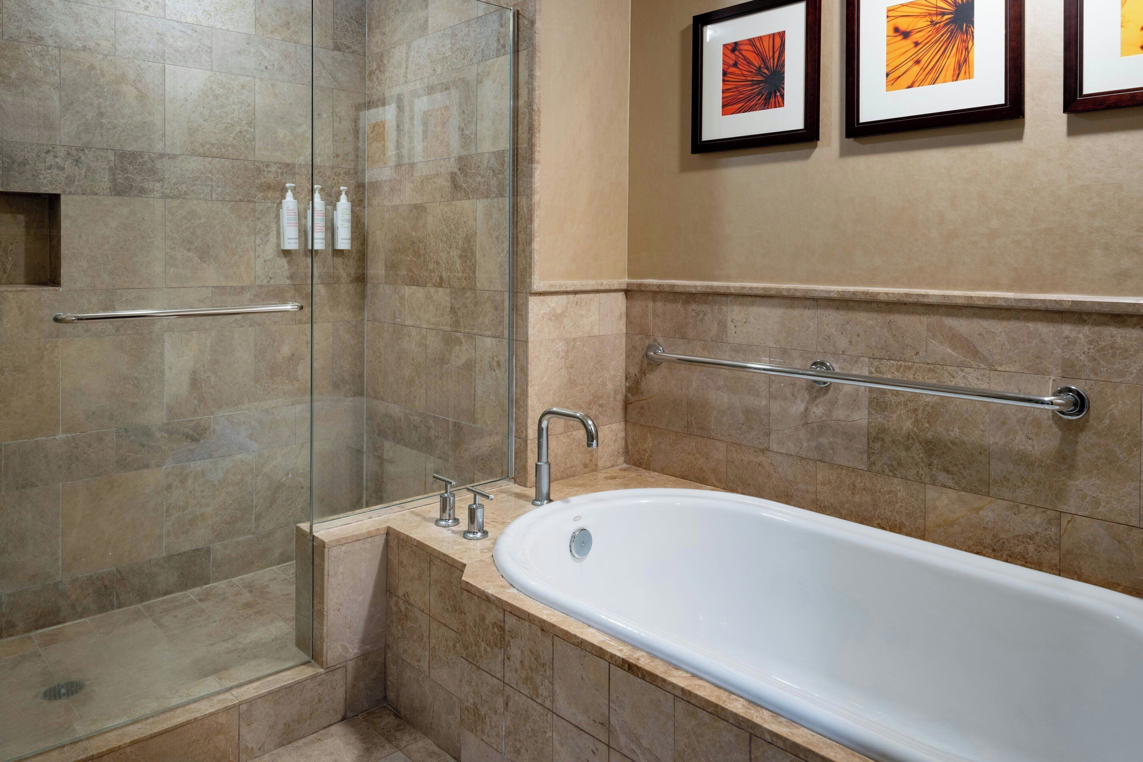 A bathroom with a glass-enclosed shower, a white bathtub, and a handrail.