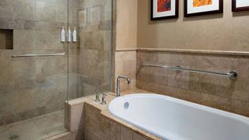 A bathroom with a glass-enclosed shower, a white bathtub, and a handrail.