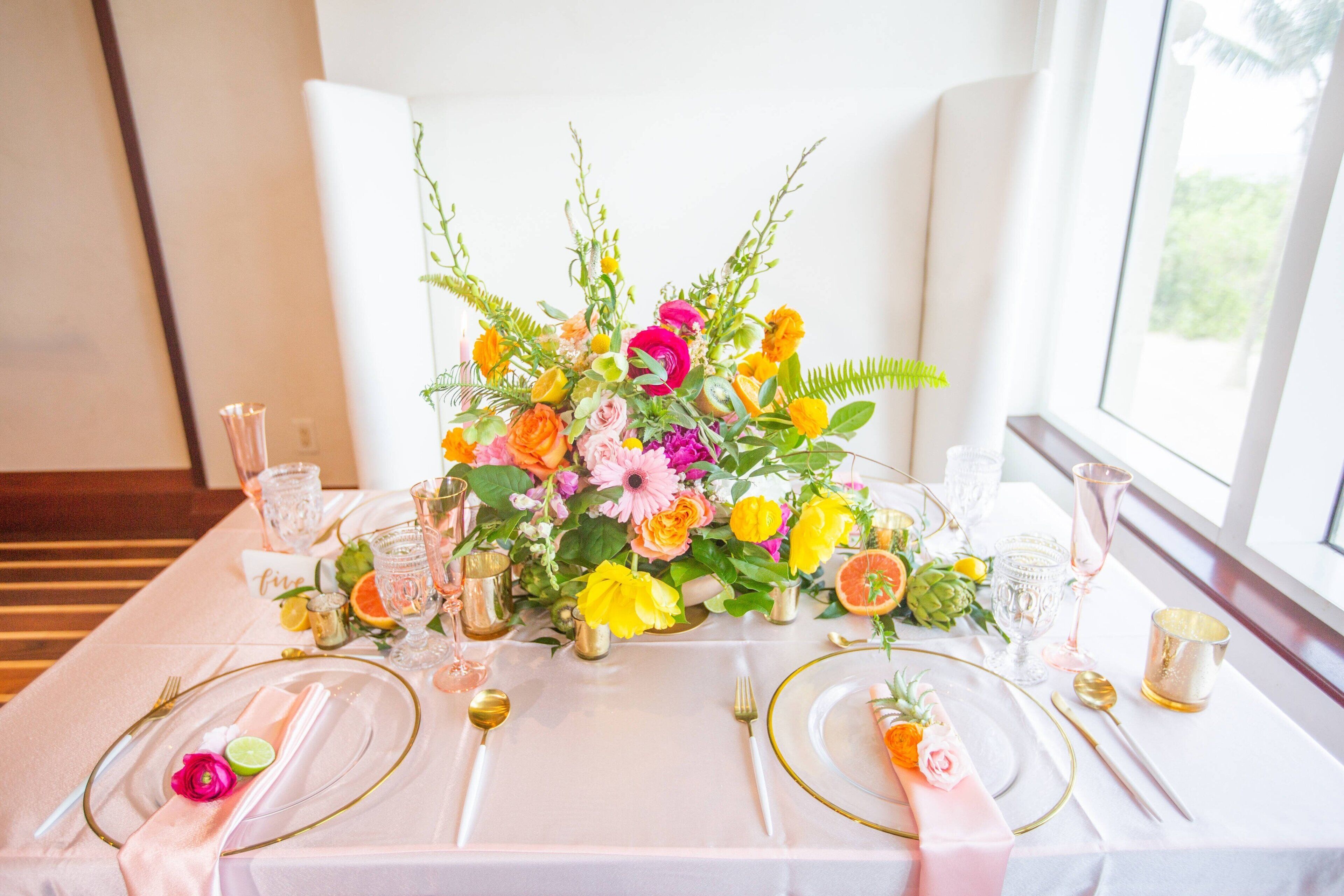Une table dressée avec une nappe blanche, des couverts dorés et un arrangement floral en guise de décoration centrale.