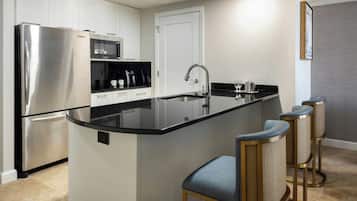 A modern kitchen with a stainless steel refrigerator, a black countertop island, and three bar stools.