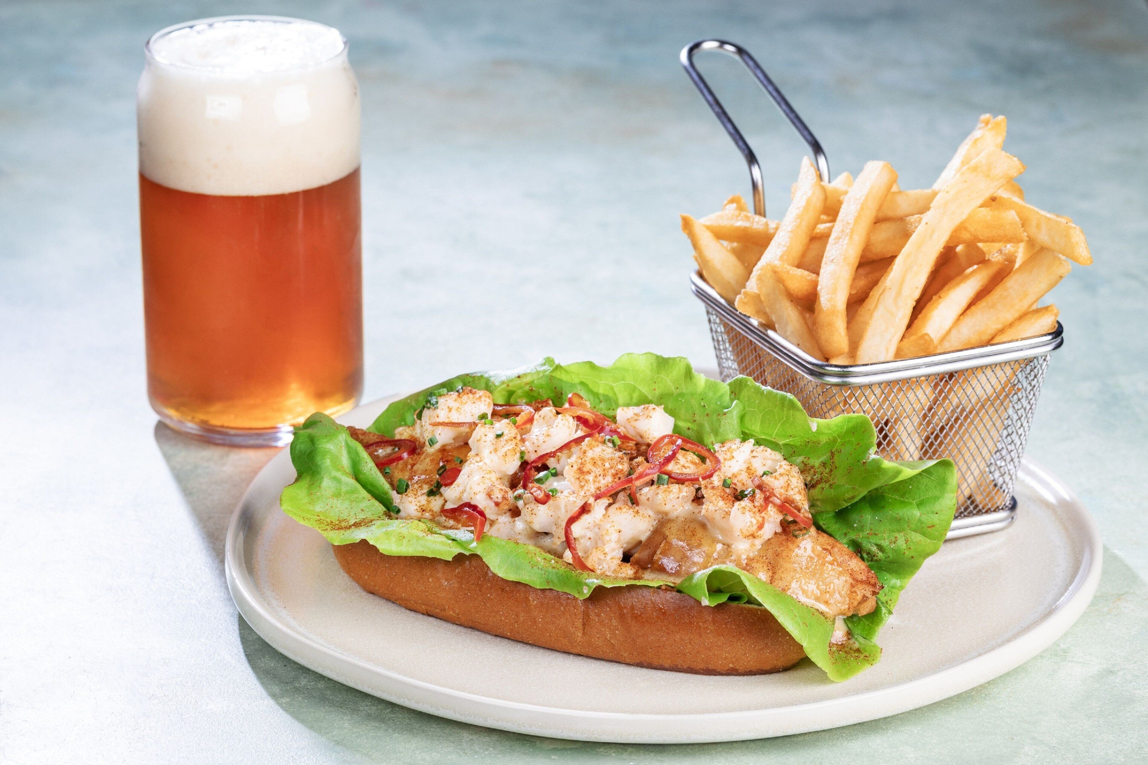 A sandwich with lettuce and a side of fries on a plate, accompanied by a glass of beer.