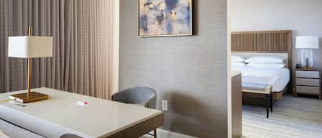A hotel room with a bed, bedside table, lamp, and a painting on the wall.