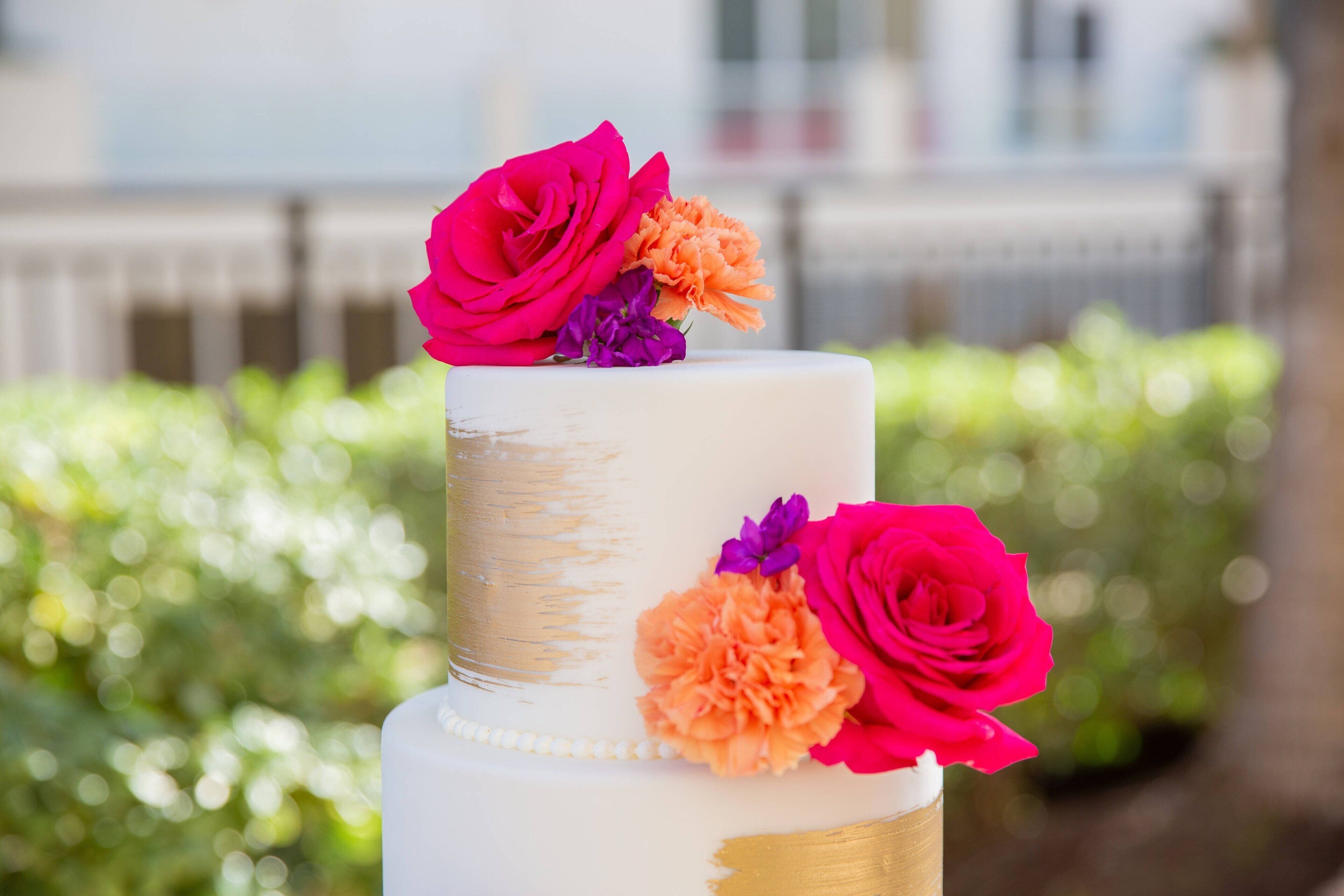 Un gâteau blanc à deux étages, agrémenté de touches dorées et de fleurs colorées sur le dessus.