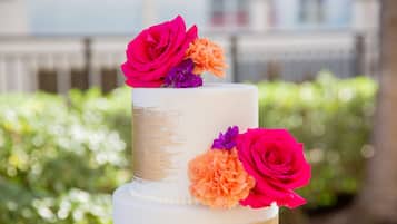 Un gâteau blanc à deux étages, agrémenté de touches dorées et de fleurs colorées sur le dessus.
