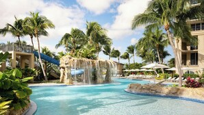 Une piscine de complexe hôtelier agrémentée d’une cascade, de palmiers et de chaises longues.