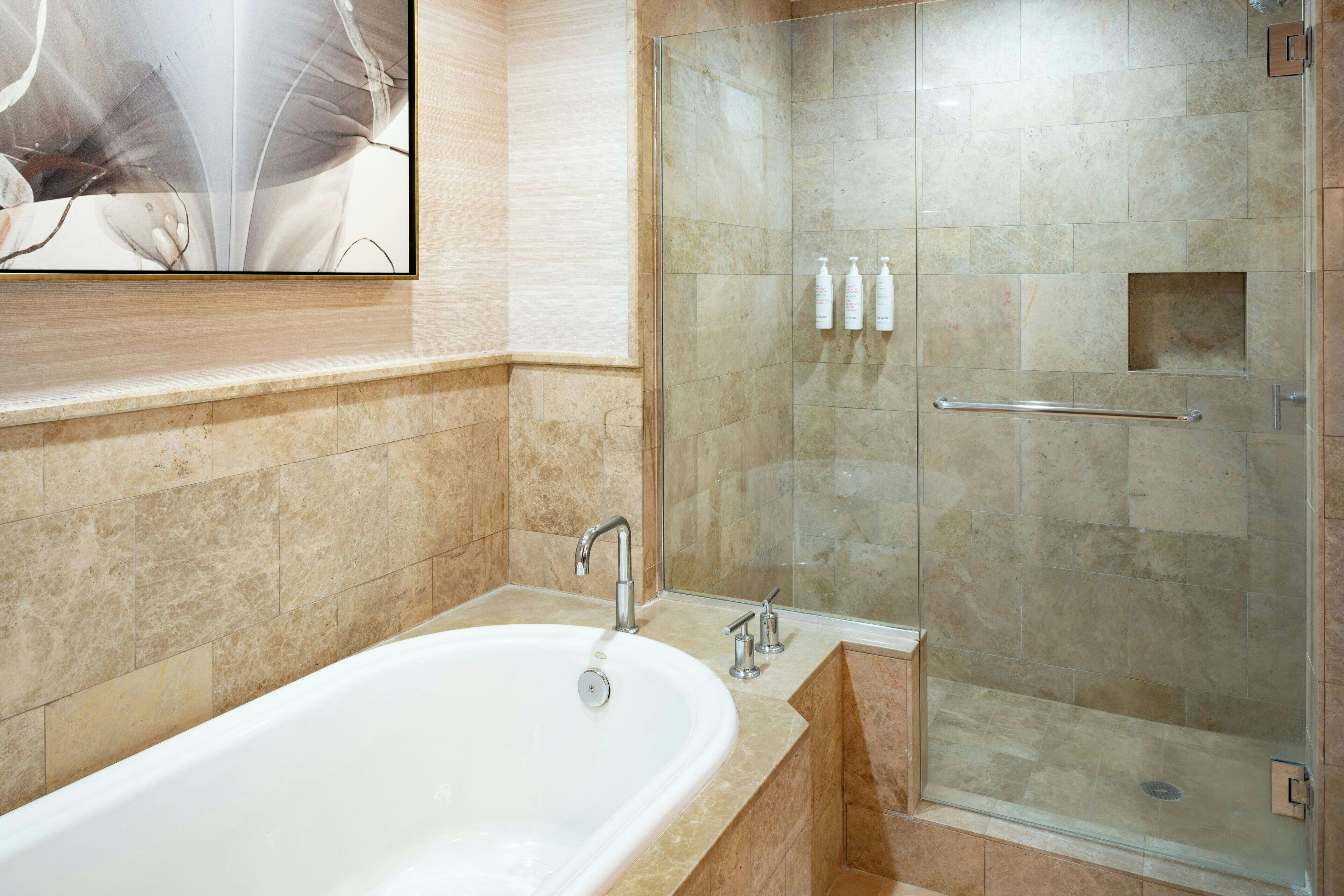 A modern bathroom with a freestanding bathtub, a glass-enclosed shower, and a marble-tiled wall.