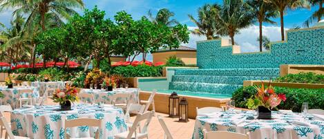 Un espace extérieur aménagé pour les repas, avec des tables rondes, des chaises blanches et une piscine en arrière-plan.