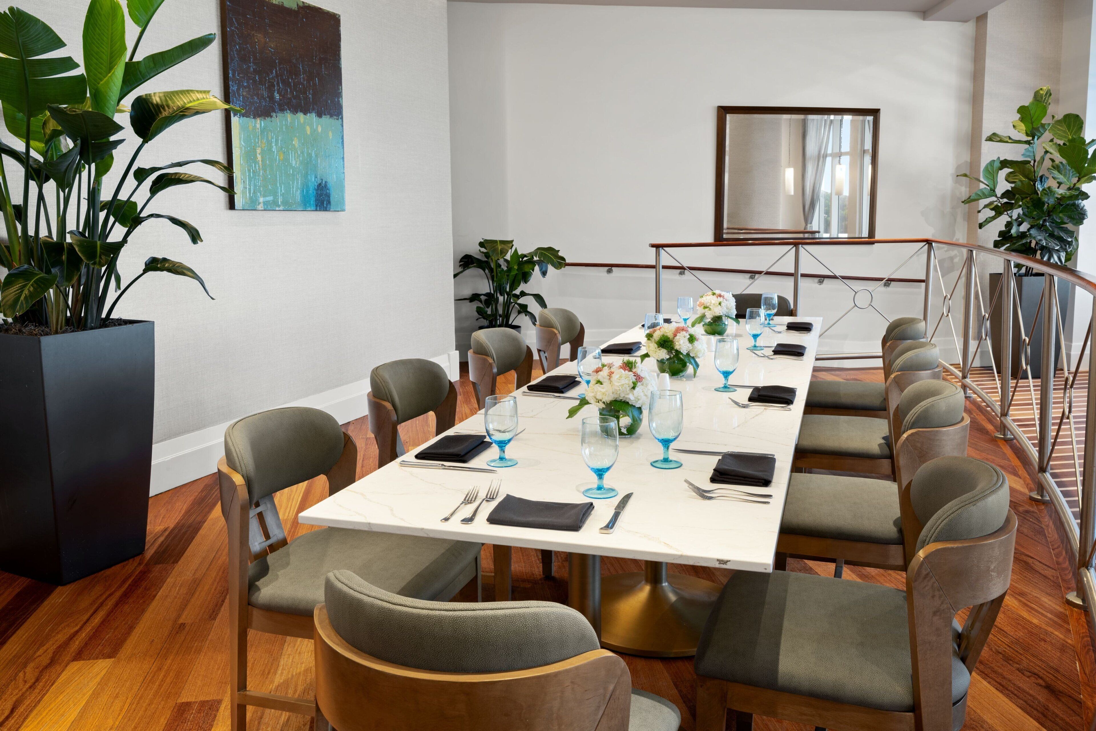 Une salle de conférence avec une longue table préparée pour une réunion, entourée de chaises, et agrémentée d’une grande plante en pot et d’œuvres d’art accrochées aux murs.