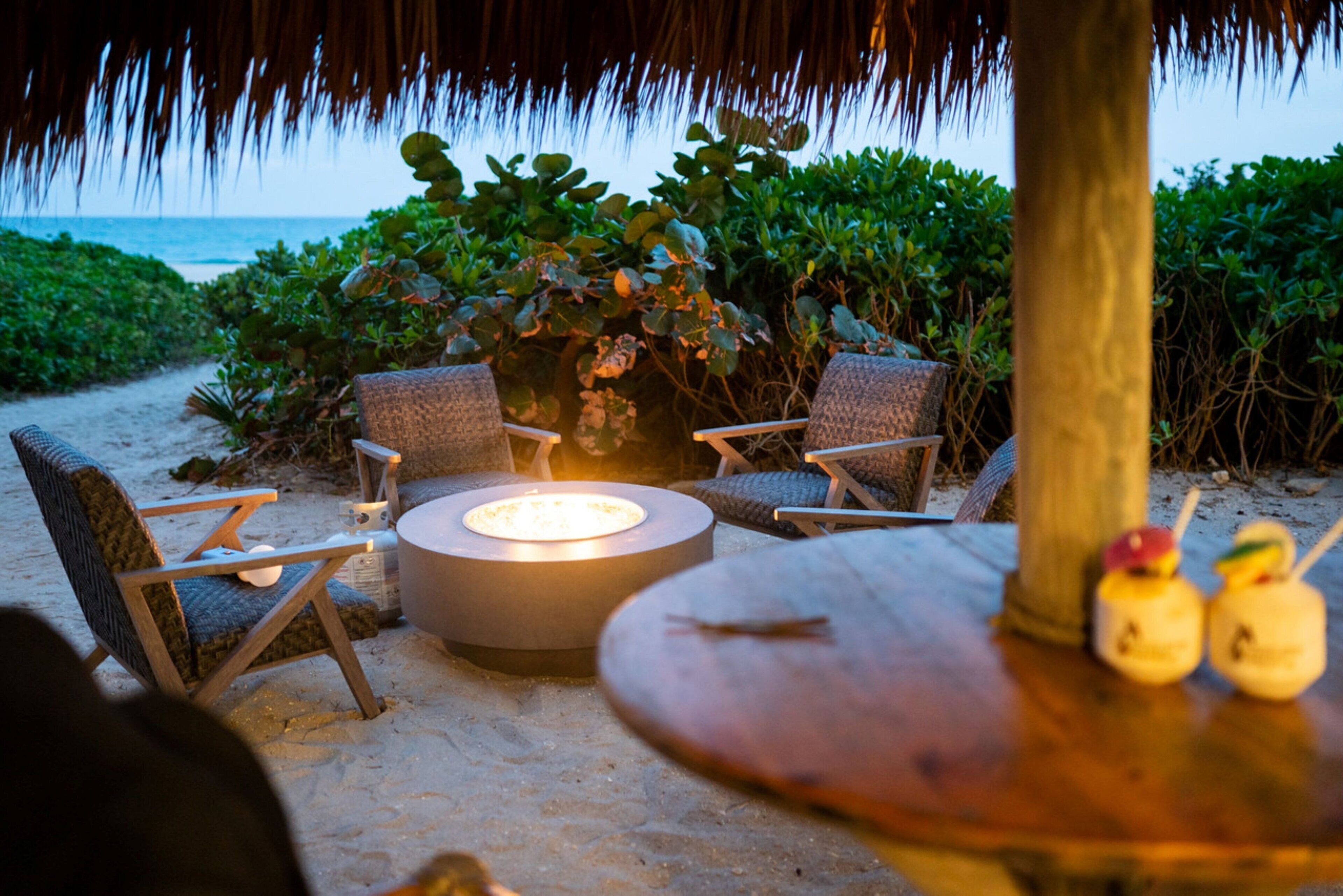 An outdoor seating area with a round table and chairs, a small fire pit, and a view of the ocean.