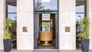 A modern building entrance with a glass door, large potted plants, and a curved ceiling structure. - View Melbourne (Melbourne)