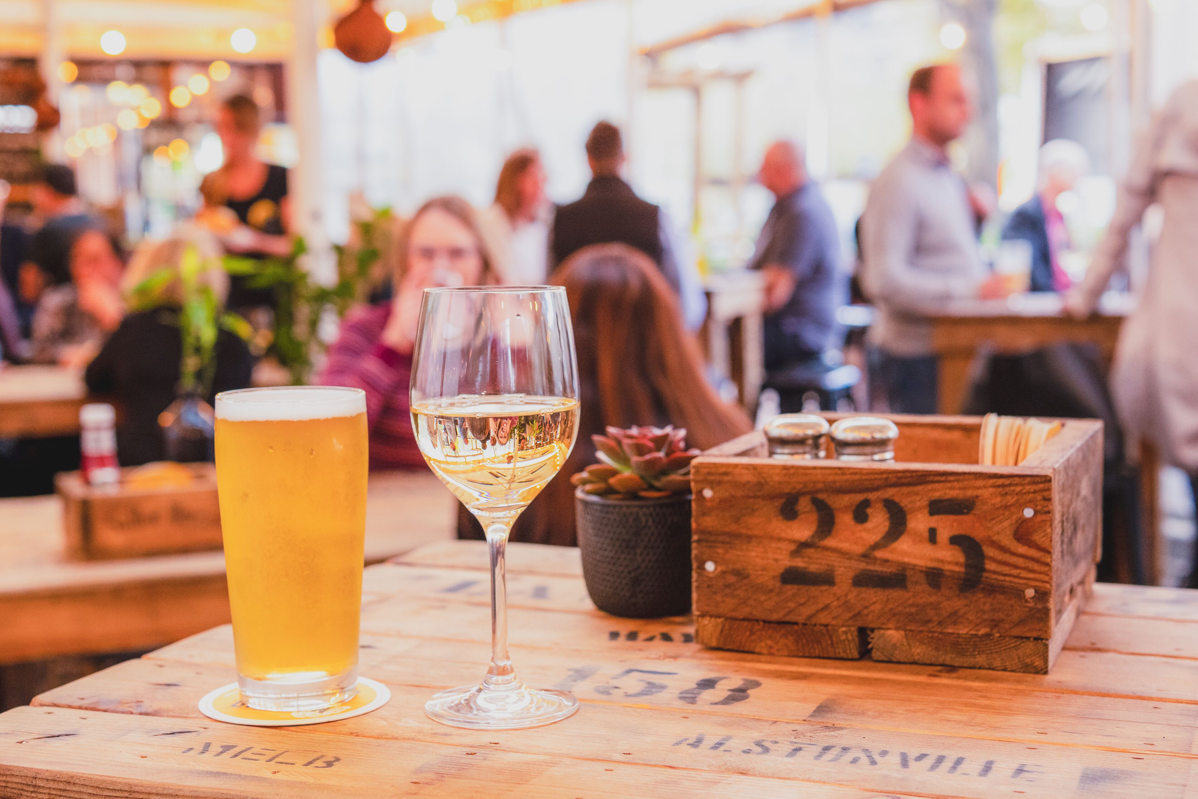 Una mesa de madera con una jarra de cerveza, un caja de madera con números y una pequeña planta en maceta.