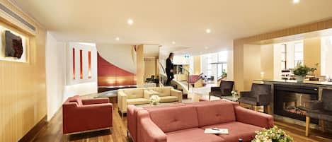 En moderne hotellobby med en rød sofa, beige lænestole og en pejs.