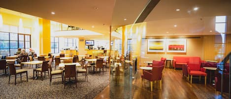 A spacious hotel lobby with multiple seating areas, a bar, and large windows offering views.