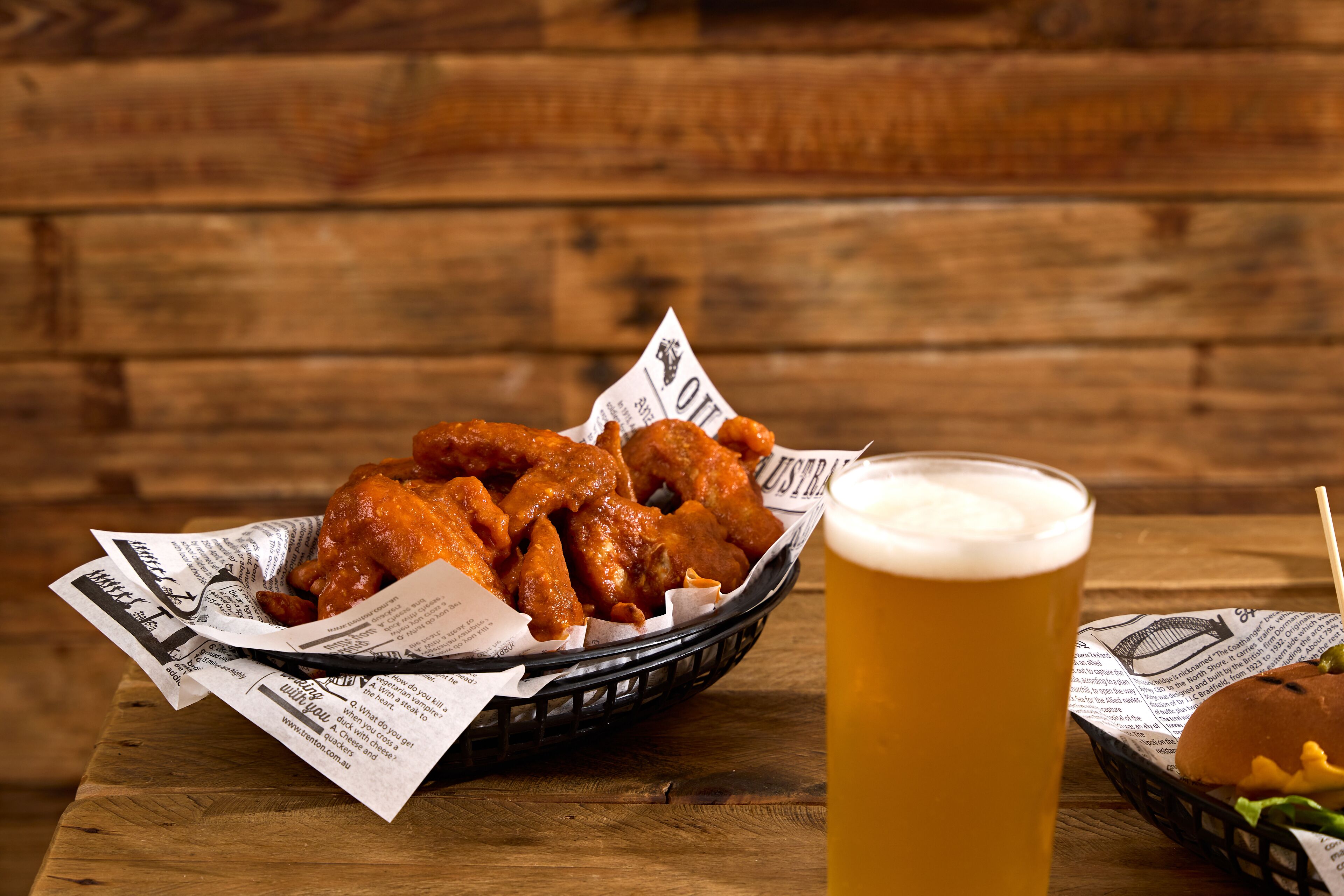 Un panier d’ailes de poulet frites, un verre de bière et un hamburger sur une table en bois.