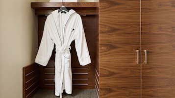 A wooden wardrobe with a mirror and a white bathrobe hanging on a rack.