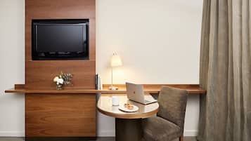 A hotel room with a wooden desk, a laptop, a lamp, and a TV mounted on the wall.