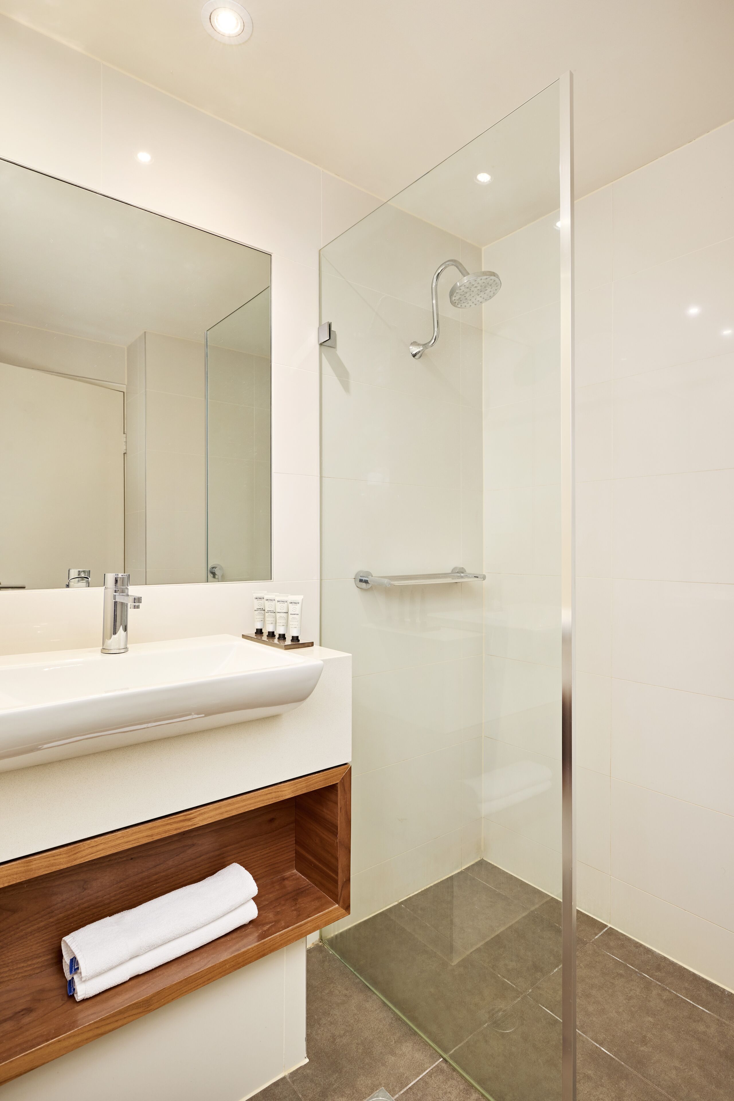 A modern bathroom with a glass-enclosed shower, a white sink with a wooden shelf, and a large mirror.