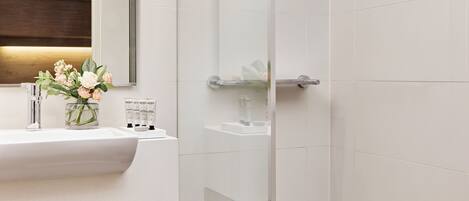 A modern bathroom with a glass shower enclosure, a white sink with a wooden shelf, and a mirror above the sink.