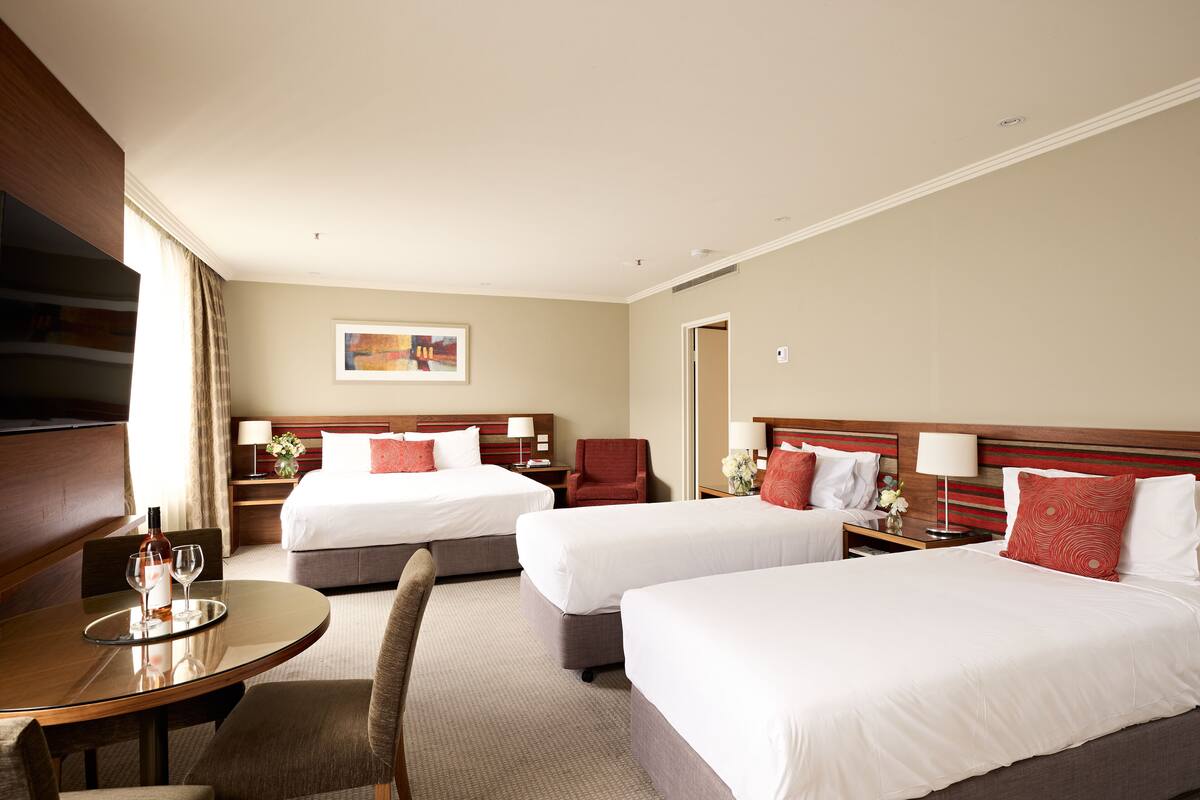 A hotel room with two beds, a dining table, and a TV.