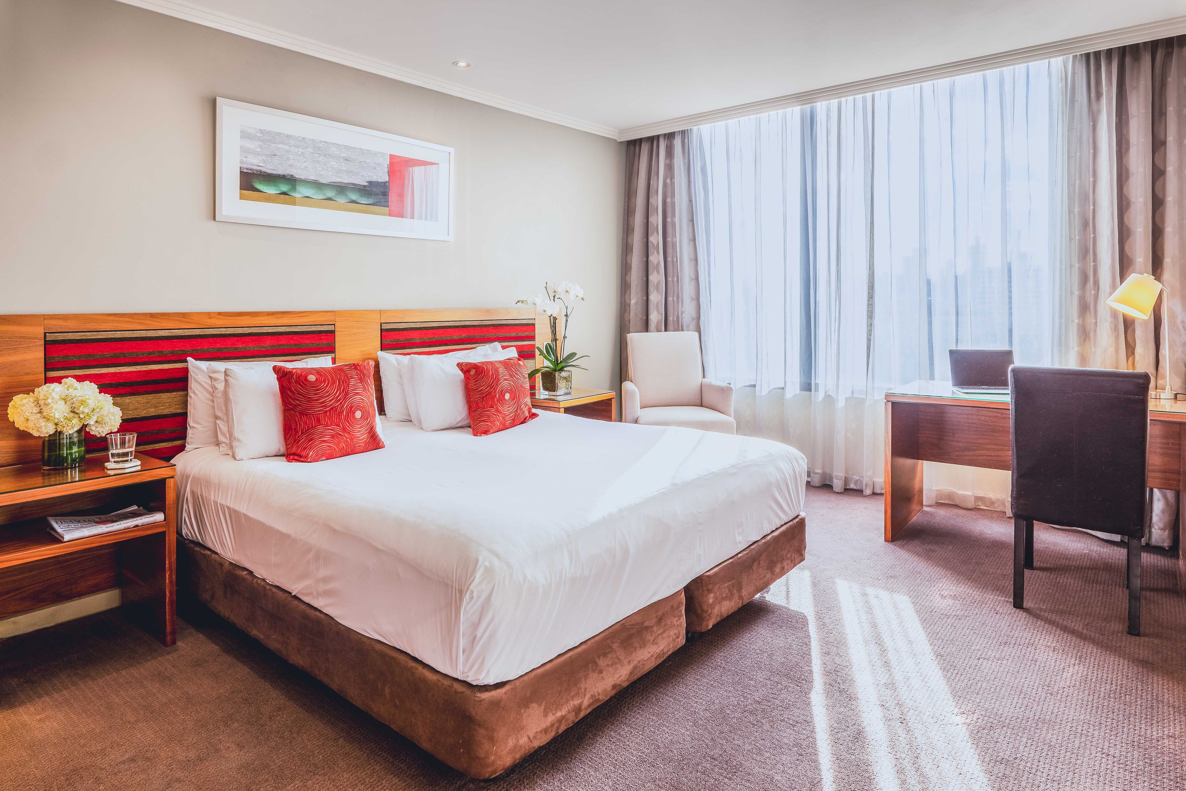 A hotel room with a large bed, a desk, a chair, and a window with curtains.
