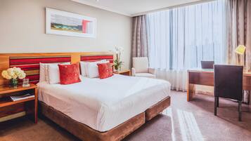 Una habitación de hotel con una cama grande, un escritorio, una silla y un ventanal con cortinas.