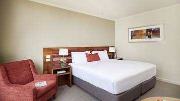 A hotel room with a bed, a red armchair, a nightstand, a lamp, and a painting on the wall.
