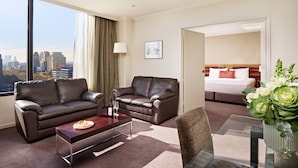 A hotel room with a city view, two leather sofas, a dining table, a bed, and a large window. - View Melbourne (Melbourne)