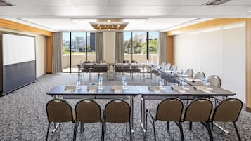 Un salón de conferencias con una larga mesa, sillas, botellas de agua y una pantalla de proyector.