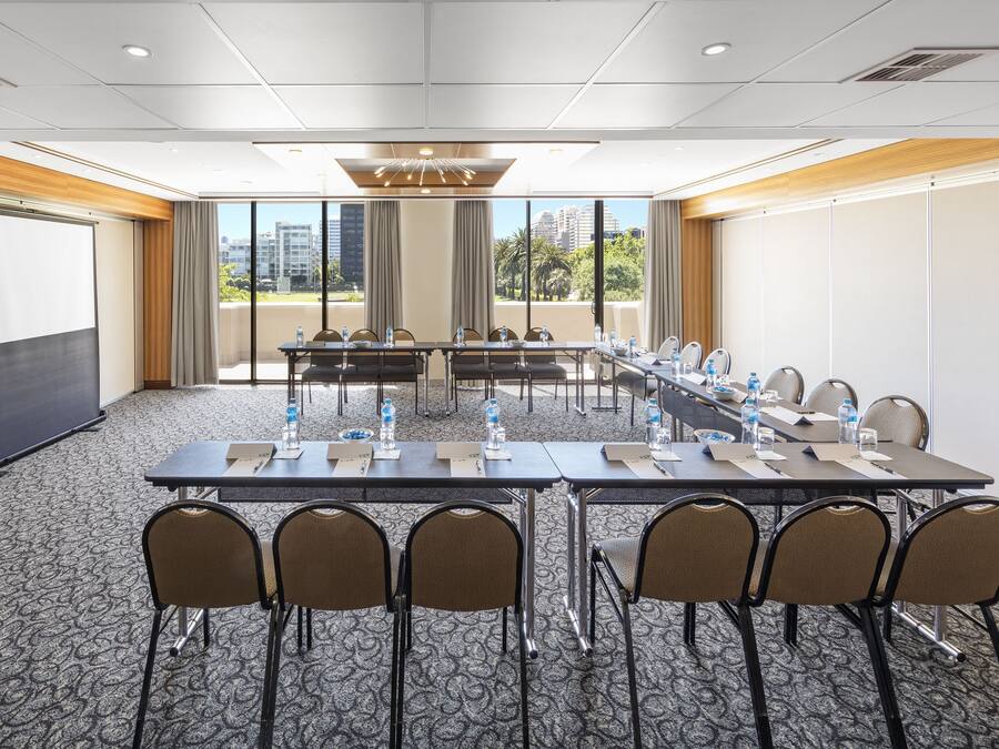 Un salón de conferencias con una larga mesa, sillas, botellas de agua y una pantalla de proyector.