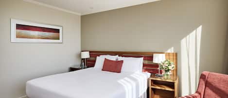Habitación de hotel con una cama grande, una mesita de noche de madera, una silla roja y un cuadro en la pared.