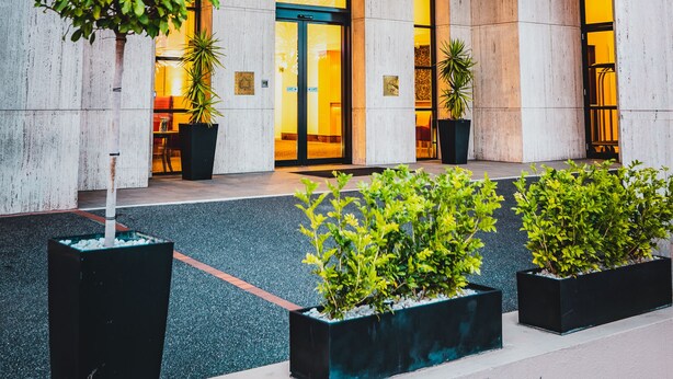 A modern building entrance with a glass canopy, large stone columns, and potted plants. - View Melbourne (Melbourne)
