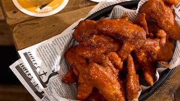 A wooden table with a glass of beer, a basket of chicken wings, and a coaster with the text "Hop Garden".