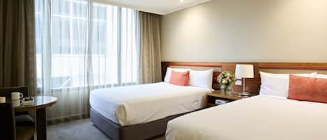 A hotel room with two beds, a desk, and a chair.