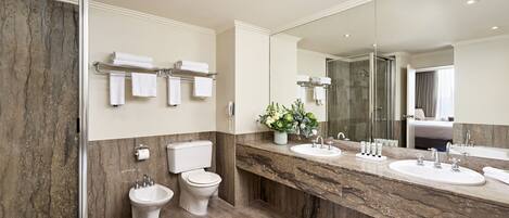 A modern bathroom with a marble vanity, two sinks, a toilet, and a shower.