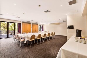 Un salón de conferencias con una larga mesa dispuesta para comer, rodeada de sillas y equipada con una estación de café.