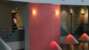 Un moderno vestíbulo de hotel con una escalera, iluminación colgante y una persona cerca de un ascensor.