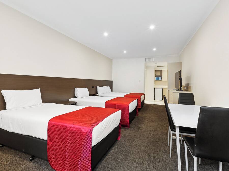 A hotel room with three beds, a dining table, and a kitchenette.