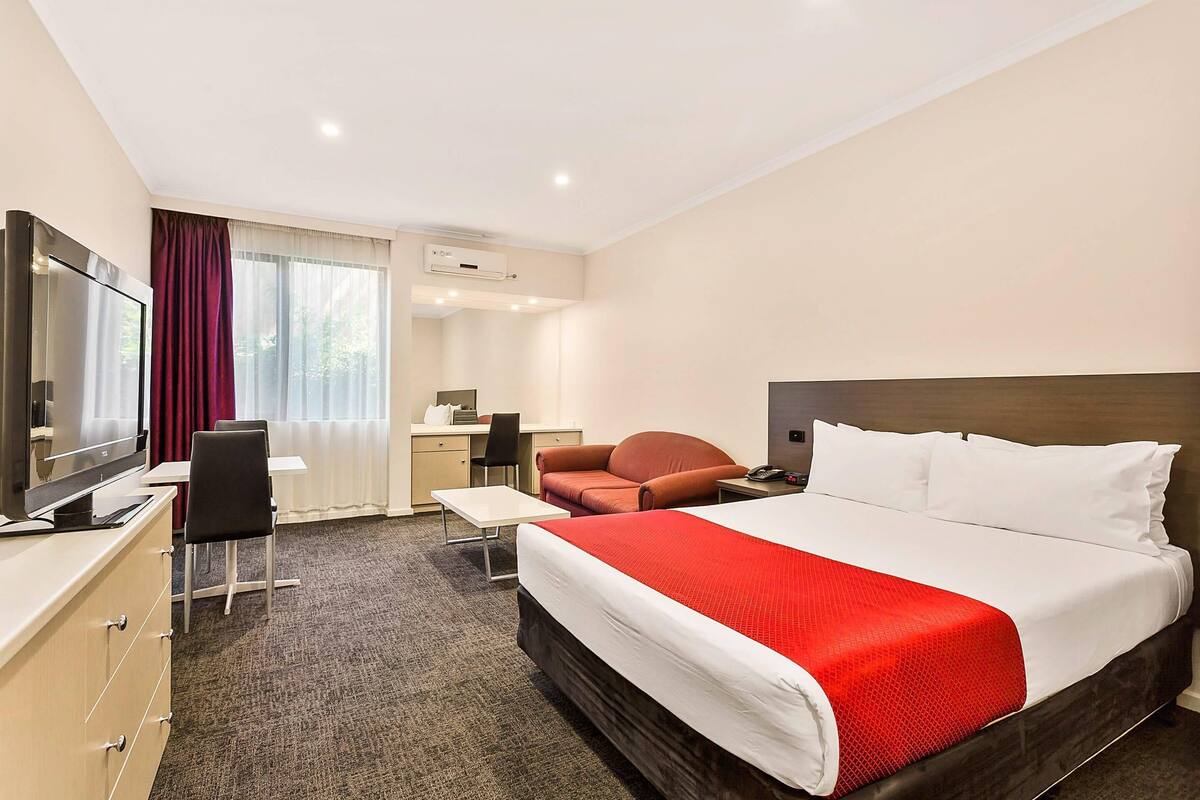 A hotel room with a bed, desk, chair, TV, and a window with curtains.