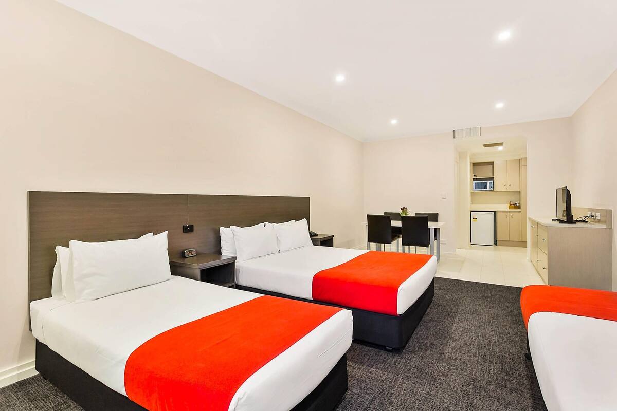 A hotel room with two beds, a desk, a chair, and a kitchenette.