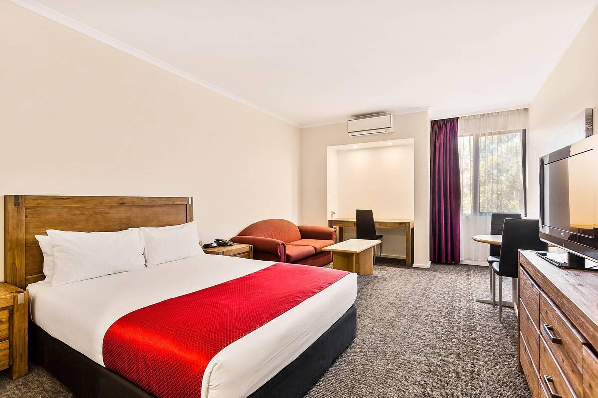 A hotel room with a bed, a desk, a chair, a TV, and a window with curtains.