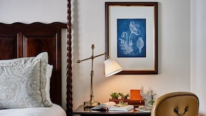A bedroom with a bed, a desk with a lamp, a framed picture, and a chair. - Deer Path Inn (Lake Forest)