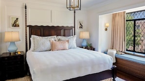 A bedroom with a large bed, two bedside tables, a window with curtains, and a chandelier. - Deer Path Inn (Lake Forest)
