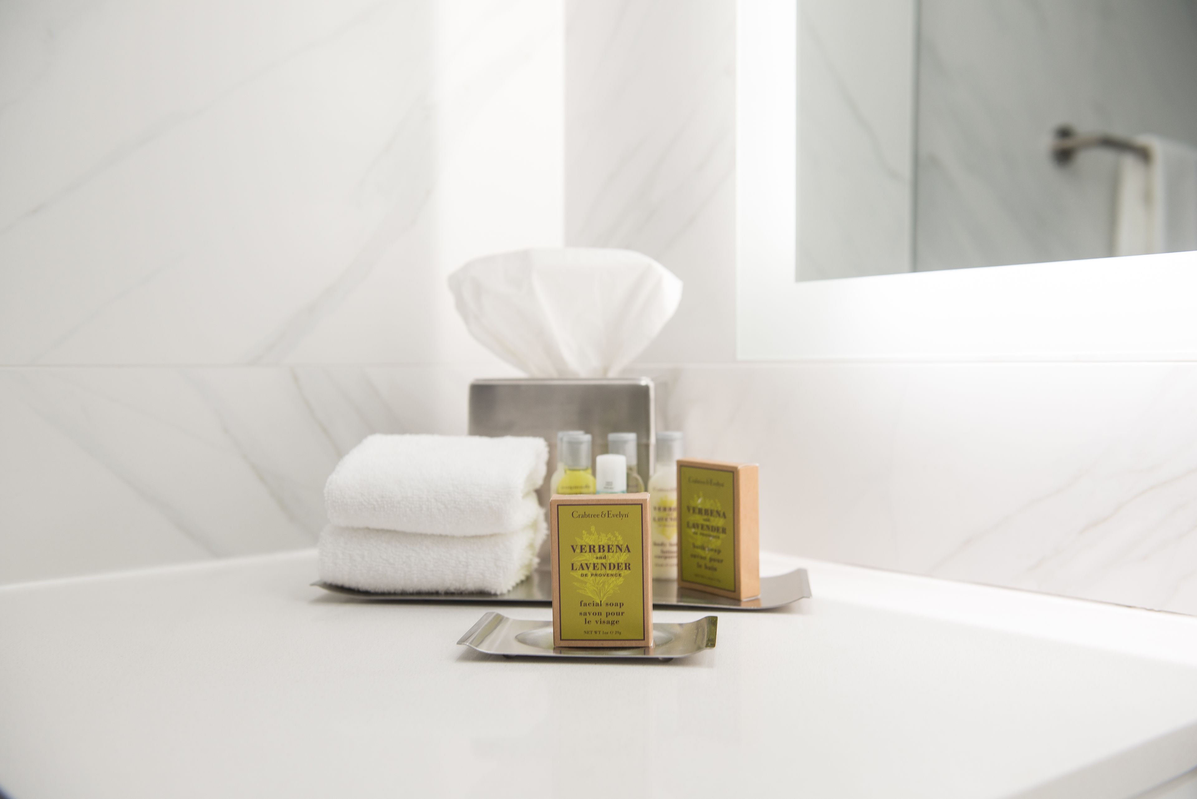 A bathroom with a white marble sink, a tissue box, and two bottles of Verbenia Lavender facial soap.