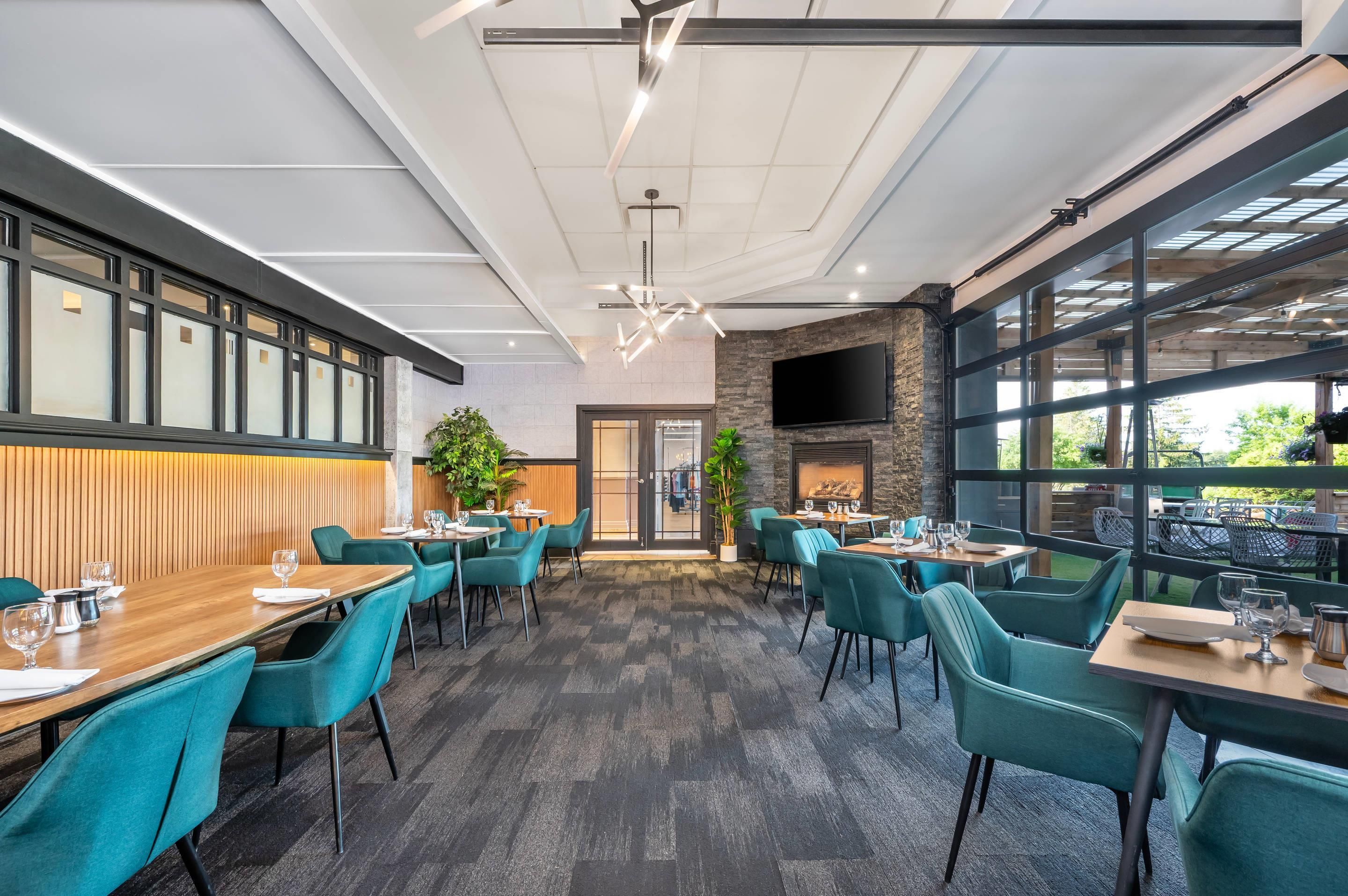Un restaurante con una decoración moderna, que presenta sillas color turquesa, mesas de madera y una pared de piedra con chimenea.