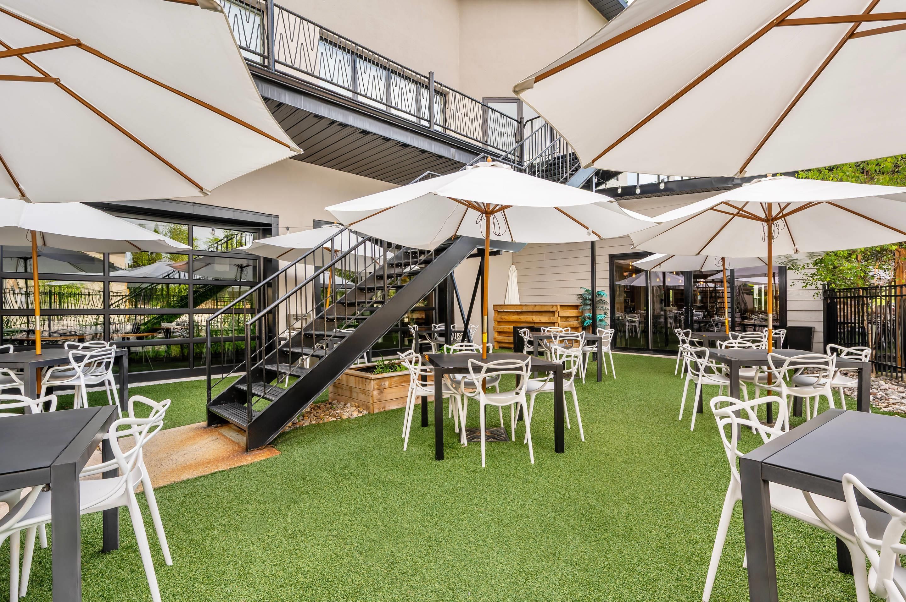 An outdoor seating area with tables and chairs, a staircase, and umbrellas.