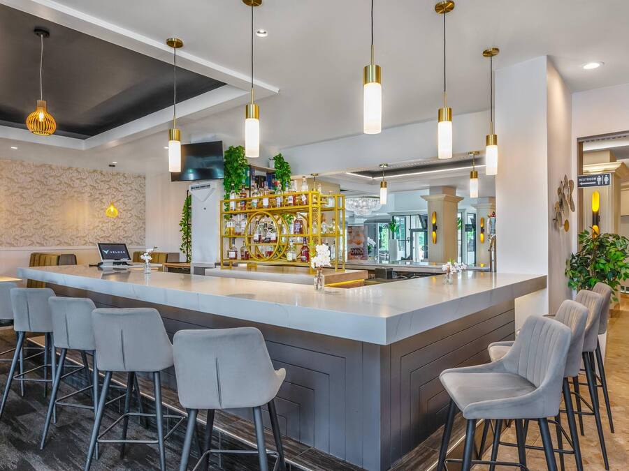 Uma área de bar moderna com uma ilha central, banquetas e luminárias pendentes.