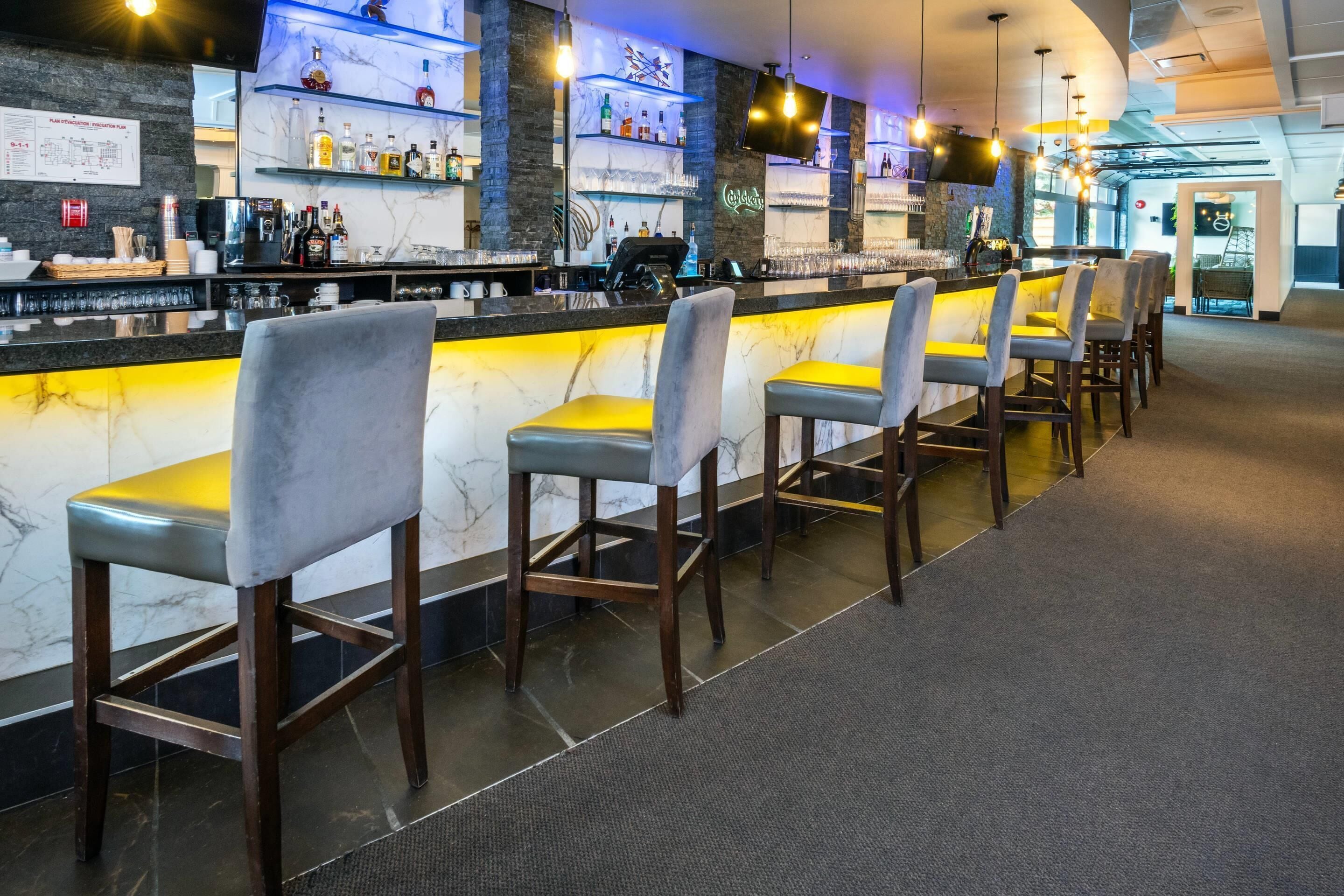 Een bar met marmeren aanrecht, barstoelen en gevulde flessenkasten.