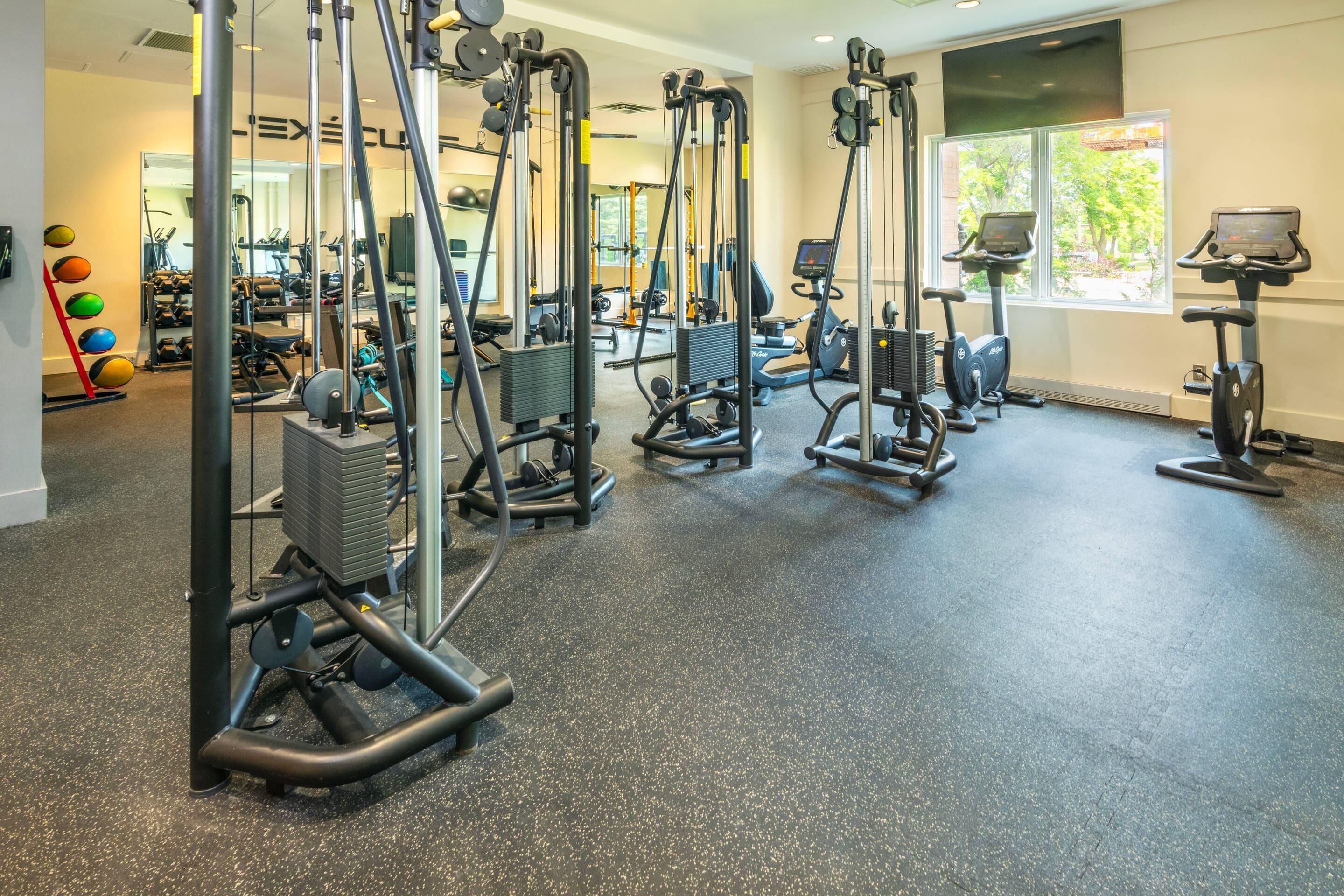 A gym with various exercise equipment, a large window, and a mirror.
