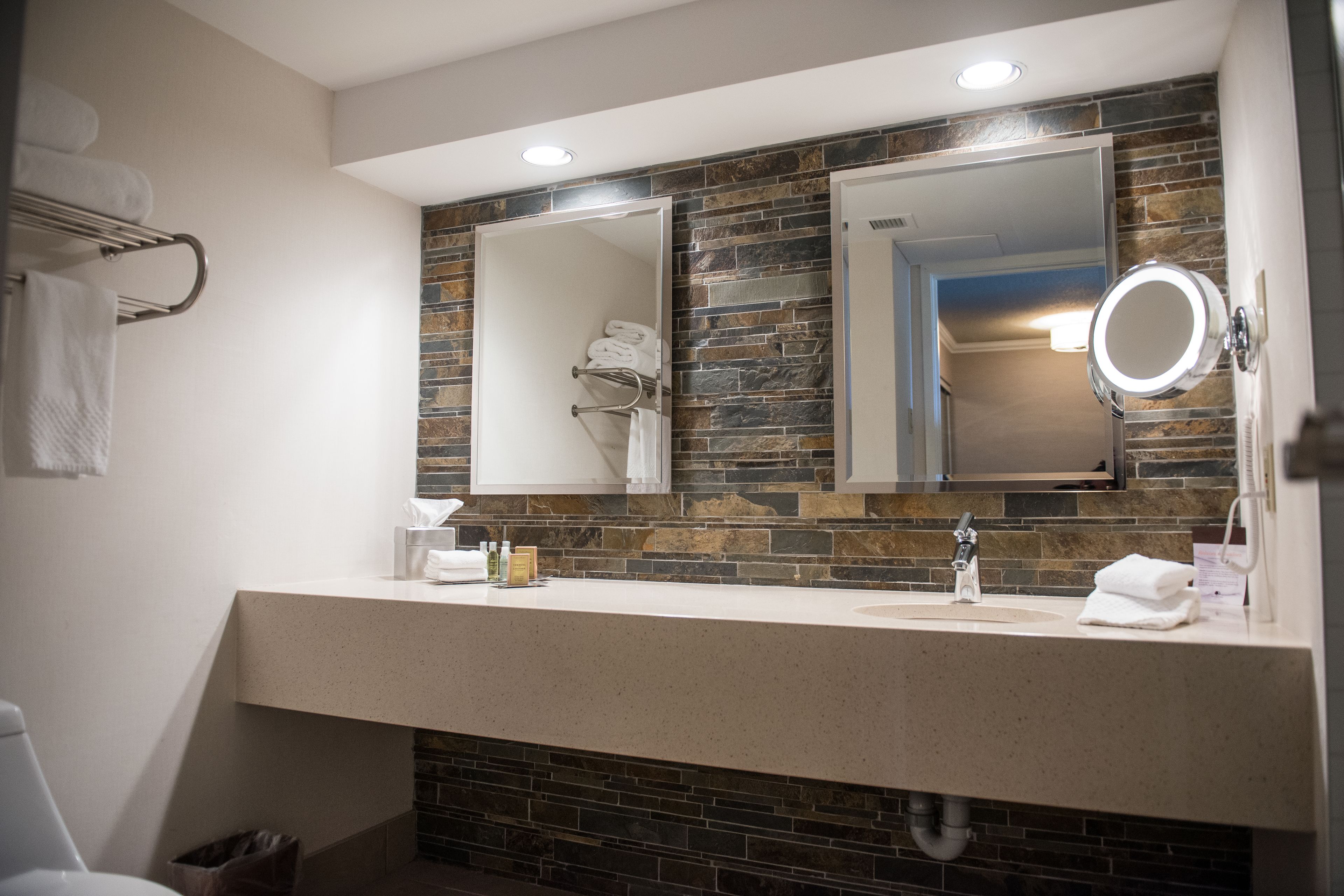 A modern bathroom with a stone backsplash, a large mirror, and a vanity with a sink.